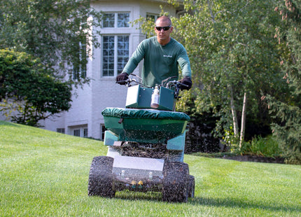 Operator riding the PermaGreen Triumph spreader sprayer up a sloped lawn while spreading fertilizer
